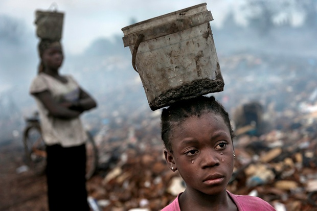 Fati, aged 8, works with other children searching through hazardous waste on an e-waste dump in Accra, Ghana.  Balancing a bucket on her head containing the metal she has found, tears stream down her face as the result of the pain from malaria.